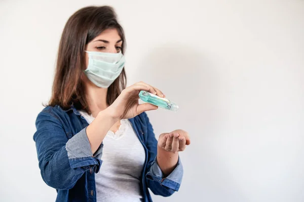 Woman with medical protection mask putting on antiseptic to disinfect her hands