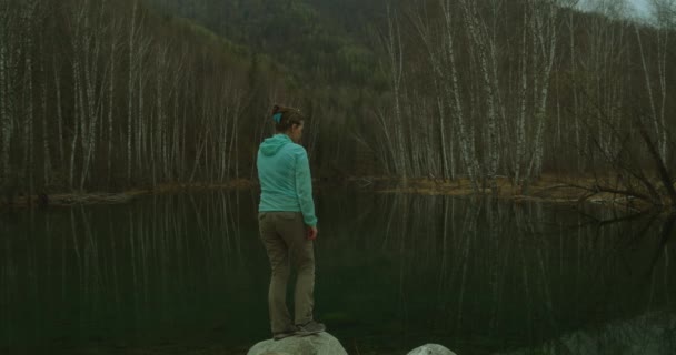 Νεαρή γυναίκα στέκεται μπροστά από μια λίμνη και κοιτάζει προσεκτικά στην απόσταση. — Αρχείο Βίντεο
