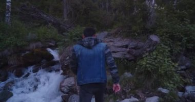 Kot elbiseli Asyalı genç bir adam dağ nehri boyunca tırmanıyor.