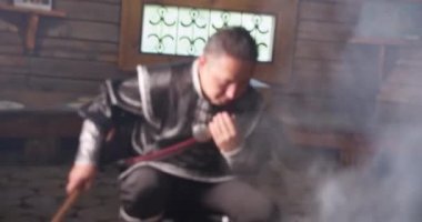 Metal mermili barbekü. Kalın duman. Ulusal kostümlü Asyalı müzisyen.