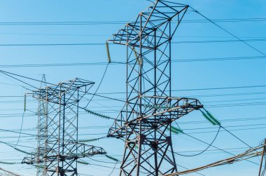 Mavi gökyüzüne karşı yüksek voltajlı elektrik direkleri.