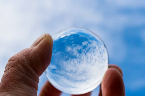 The hand of a psoriasis patient holds a glass ball in which a blue sky with clouds is reflected. A symbol of hope for recovery. International Psoriasis Day.