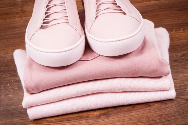 Pink leather shoes and stack of clothing for woman lying on rustic boards