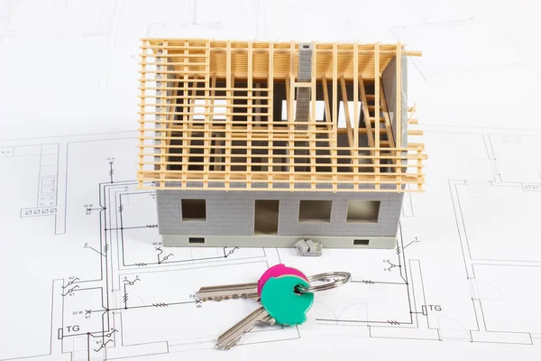 Small house under construction and home keys lying on electrical drawings for project, concept of building home
