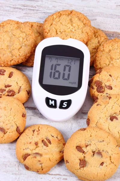 Glucose meter with bad result of measurement sugar level and heap of cookies, concept of diabetes, healthy lifestyles and reduction eating sweets