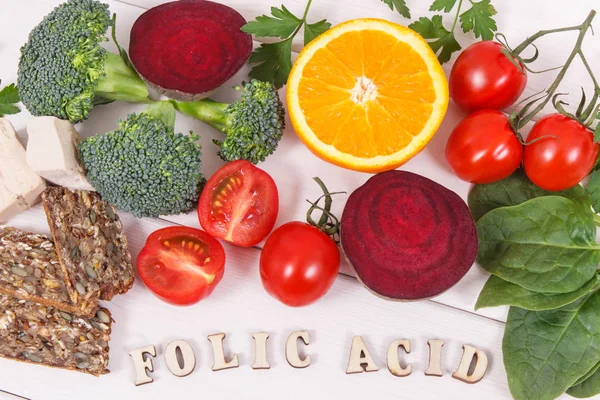 Inscription folic acid with nutritious products containing vitamin B9, natural sources of minerals and folic acid, concept of healthy nutrition