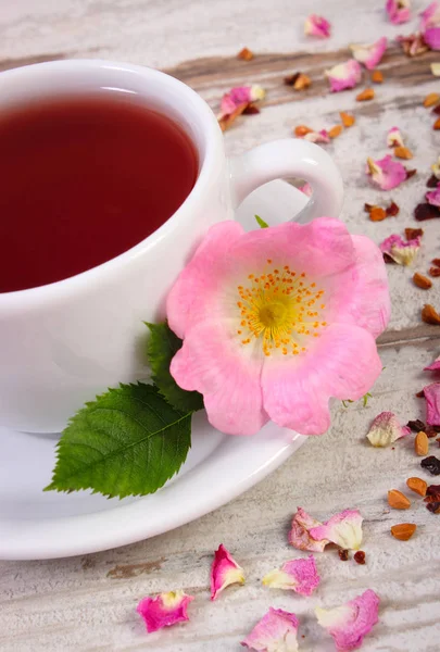 Taze çiçek çiçek açan ve kurutulmuş yaprakları eski tahta üzerinde çay tahıllar ile yabani gül desenli, sıcak çay