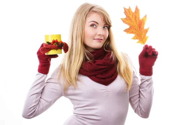 Smiling girl wearing woolen shawl and gloves, holding autumnal leaf and cup of hot tea with autumn decoration, warming drink, white background
