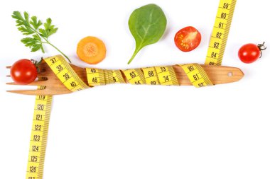 Tahta çatal sarılı mezura ve beyaz arka planda taze olgun sebzeler, kilo verme ve sağlıklı beslenme kavramı