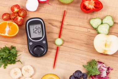 Şeker seviyesi ve olgun meyvelerden yapılmış saat ile vitamin içeren sebzeler ve akşam yemeği için zaman gösteren glikoz ölçer.