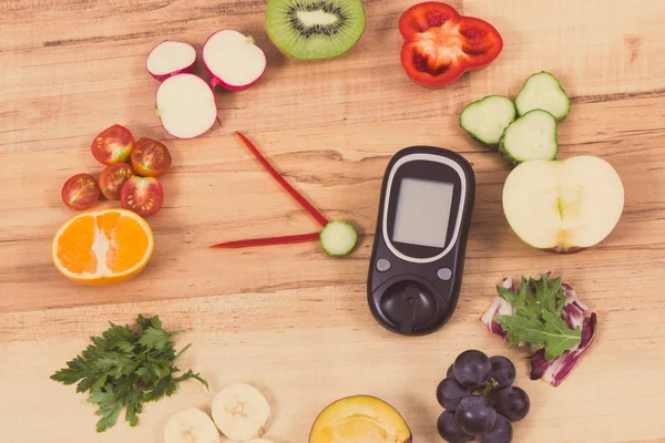 Glucose meter for checking sugar level and fresh ripe fruits with vegetables in shape of clock, concept of healthy food for diabetics