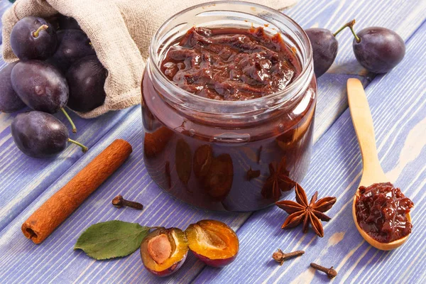 Fresh homemade plum marmalade in jar, ripe fruits and spices on wooden boards, concept of healthy sweet dessert
