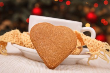 Gingerbread, sıcak çay veya kahve beyaz Kupası arka planda yün atkı ve Noel ağacı ışıkları ile sarılmış