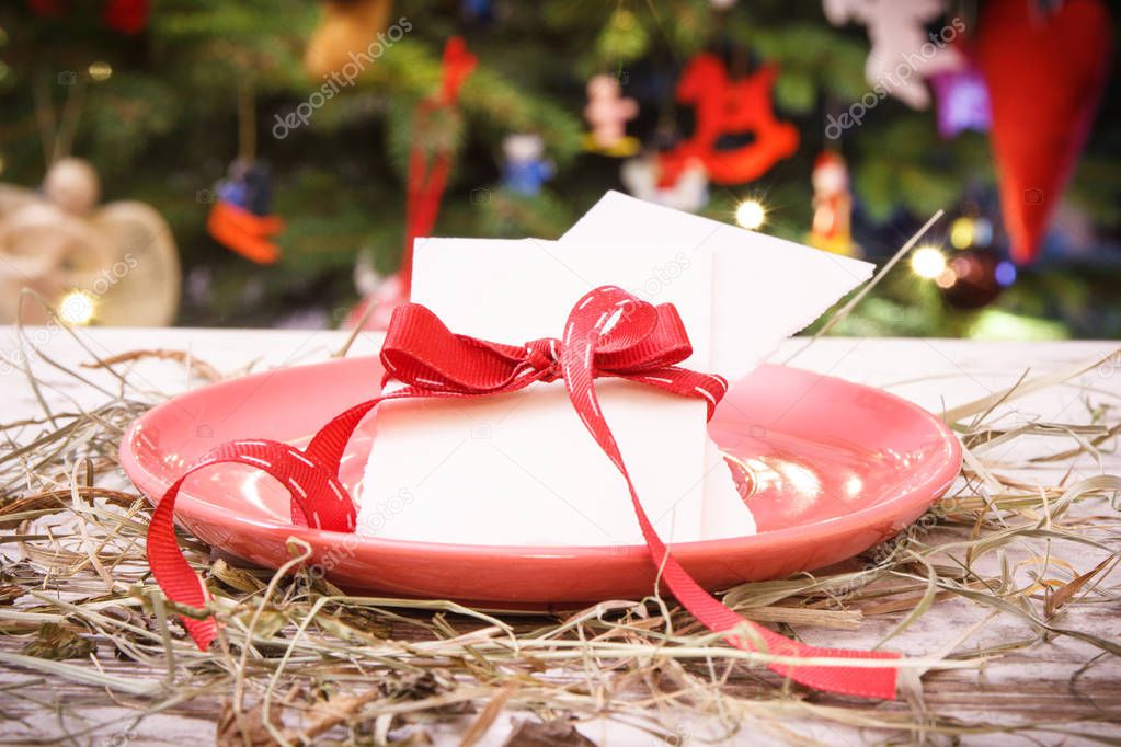 Traditional xmas eve wafer on table with hay and christmas tree with lights and decoration in background, christmas time concept