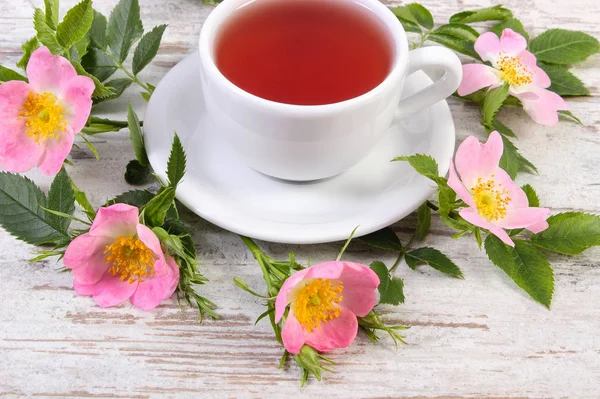 Kopje thee en wild rose bloem op oude rustieke bord — Stockfoto