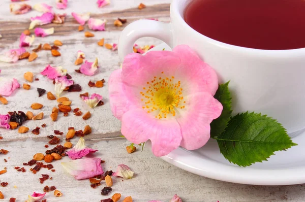 Kopje warme thee met wild rose bloem op oude rustieke houten achtergrond — Stockfoto