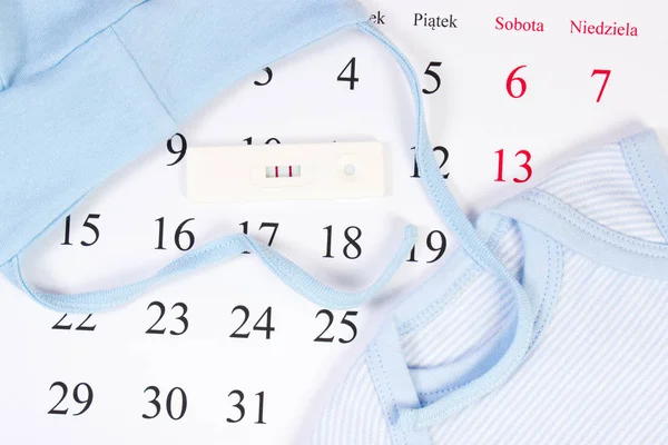 Test di gravidanza e abbigliamento per neonato sul calendario, in attesa per il bambino — Foto Stock
