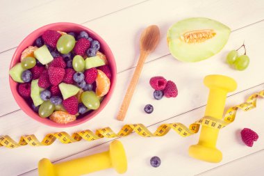Taze meyve salatası ve santimetre dambıl, sağlıklı yaşam ve beslenme kavramı ile
