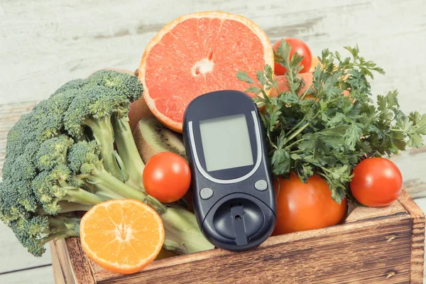 Glucose meter for chcecking sugar level and fruits with vegetables in wooden box. Diabetes, diet and slimming concept