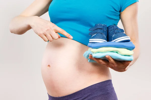 Mujer embarazada mostrando ropa para recién nacidos, esperando concepto de bebé — Foto de Stock