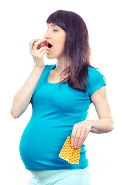Щаслива вагітна жінка їсть яблуко і тримає медичні таблетки або добавки — стокове фото