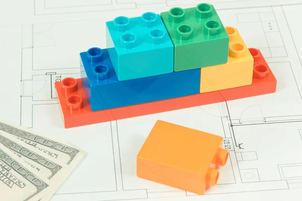 Coloridos bloques de juguetes, monedas dólar y plan de construcción de viviendas. Concepto de construcción, compra o alquiler de viviendas — Foto de Stock