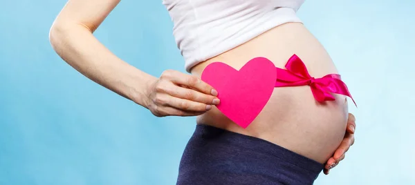 Woman in pregnant with pink ribbon on belly holding heart, concept of expecting for girl — Stock Photo, Image