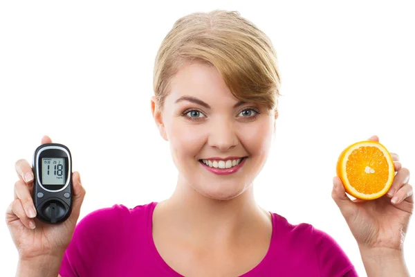 Happy woman holding glucometer and fresh orange, measuring and checking sugar level, concept of diabetes — Stock Photo, Image