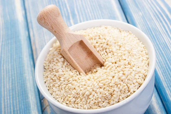 Sesame seeds with wooden scoop in white bowl on boards — Stock Photo, Image