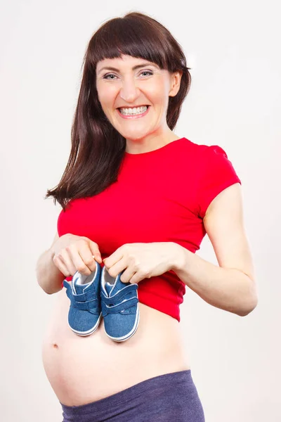 Счастливая беременная женщина с детской обувью, ожидающая ребенка — стоковое фото