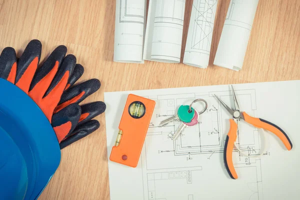 Home keys with electrical drawings, protective blue helmet with gloves and orange work tools, concept of building home
