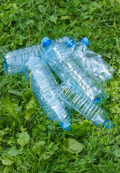 Plastic bottles of mineral water on grass in park, littering of environment concept