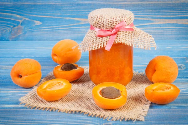 Fresh apricot marmalade in jar and ripe fruits on blue boards, healthy sweet dessert concept