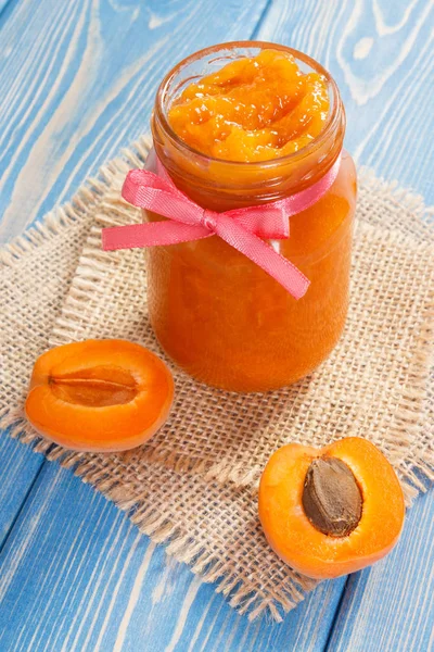 Apricot marmalade or jam in glass jar and fruits on blue boards, sweet dessert concept