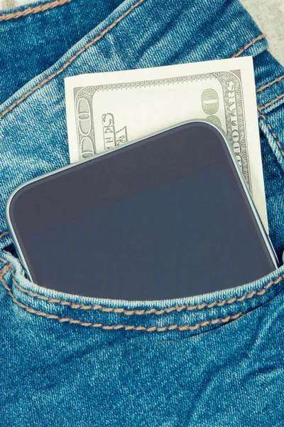 ジーンズのポケットに支払うキャッシュレスのための通貨ドルと携帯電話。金融・銀行業 — ストック写真