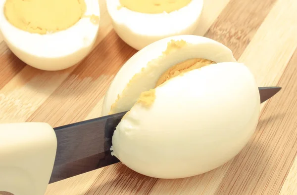 Kitchen knife cutting cooked egg on board — Stock Photo, Image