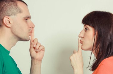 Kadın ve adam dudaklarına parmak tutarak ve sessizlik işareti gösteren