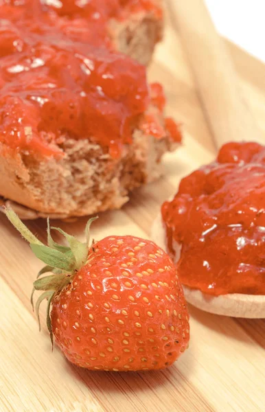 Strawberry jam on wooden spoon and wheat or rye bread in background — Stock Photo, Image