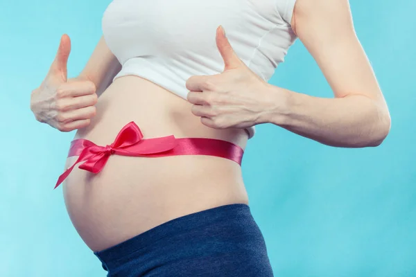 Zwangere vrouw met roze lint toont duimen omhoog. Verwacht voor pasgeboren meisje concept — Stockfoto