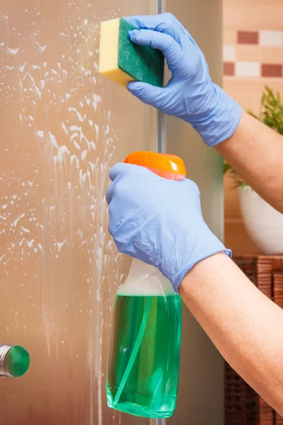 Main de femme âgée utilisant une éponge avec un détergent pour nettoyer la douche en verre, concept de tâches ménagères — Photo