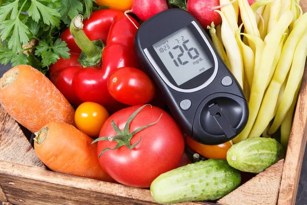 Glucose meter with sugar level and fresh ripe vegetables in wooden box as healthy snack containing vitamins