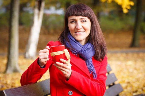 微笑在秋天公园、 喝热饮料茶或咖啡的女人 — 图库照片