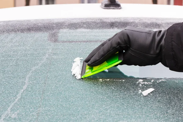 Hand holding green scraper and removing ice or snow from car window — Stock Photo, Image