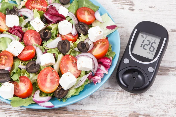 Glucometer with result of sugar level and fresh greek salad with feta cheese and vegetables. Best healthy food for diabetics, dieting and slimming