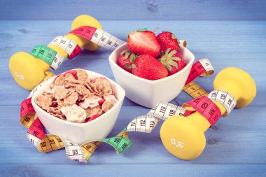 Buğday ve çavdar gevreğiyle taze olgun çilekler, fitness ve mezura için dambıllar, zayıflama konsepti, spor, sağlıklı yaşam tarzı