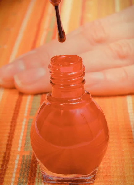 Bottle of red nail polish and hand of woman in background. Care of hands concept