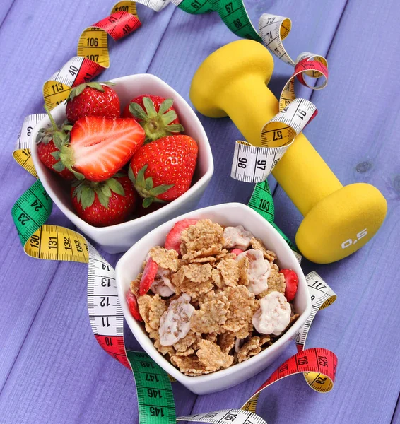 Buğday ve çavdar gevreğiyle taze olgun çilekler, fitness ve mezura için dambıllar, zayıflama konsepti, spor, sağlıklı yaşam tarzı