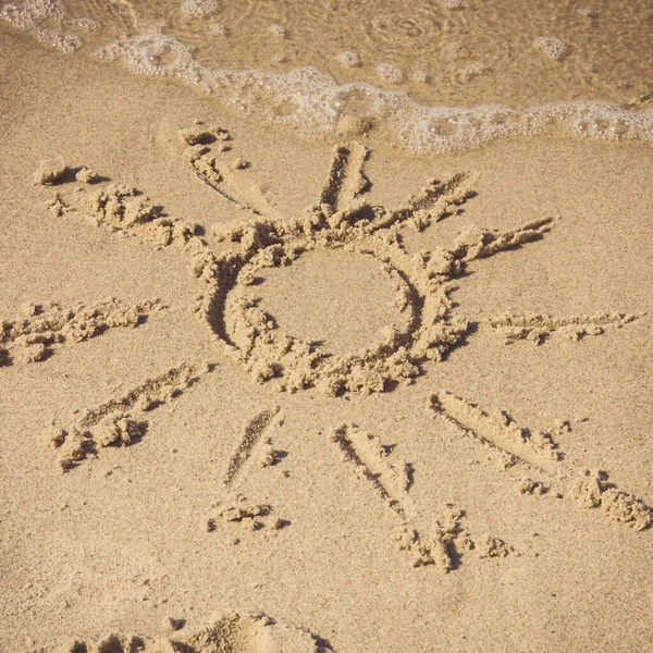 Shape of sun on sand at beach and incoming sea wave. Concept of summer, vacation time and tourism