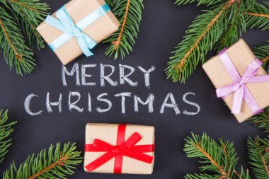 Yazılı Mutlu Noeller, siyah arka planda yeşil ladin dalları ve kurdeleli hediyeler. Noel zamanı için dekorasyon