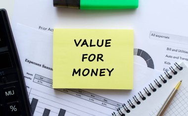 Beyaz bir arka planda, ofis malzemelerinin yanında para karşılığı VALUE mesajı olan bir not. Kalem ve hesap makinesi. İş konsepti.
